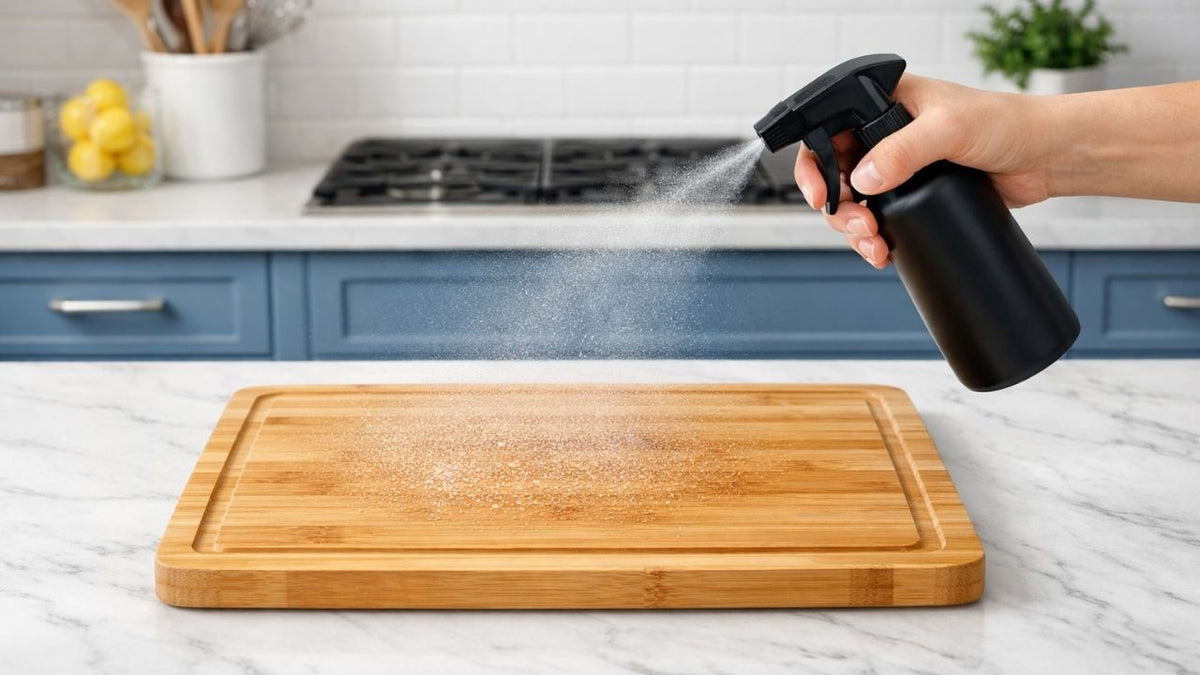 Hypochlorous acid surface cleaner being sprayed onto a bamboo cutting board on a white marble kitchen counter