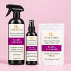 River Refresh Hypochlorous Acid Spray Facial Cleanser Starter Kit set including a 16 oz spray bottle, a 4 oz spray bottle, and a 16 oz activation packet, all in black packaging with white and purple labels, set against a solid pink background.