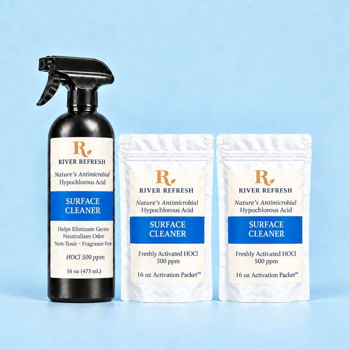 A black 16oz spray bottle labeled River Refresh Surface Cleaner 32oz Starter Kit stands next to two white pouches of River Refresh Surface Cleaner activation packets on a light blue background.